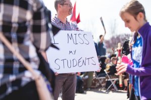 teacher holding a sign that reads "I miss my students".