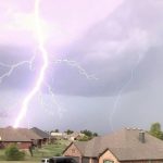 A bolt of lightning striking behind houses
