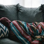 A person napping on the couch with a blanket over them