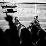 Two people singing while others put their hands up in worship